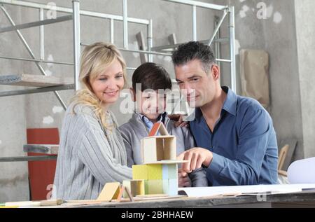 Bambini felici e la sua famiglia che gioca a costruire una casa con modelli di costruzione in sito interno. Casa acquistare e costruire obiettivo concetto Foto Stock