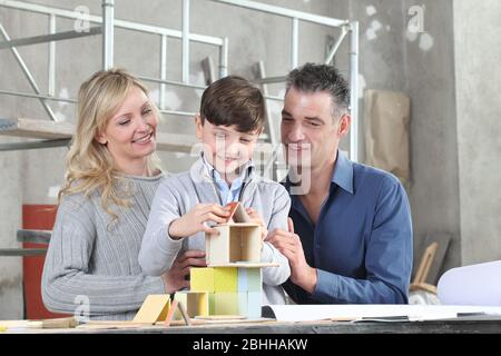 Bambini felici e la sua famiglia che gioca a costruire una casa con modelli di costruzione in sito interno. Casa acquistare e costruire obiettivo concetto Foto Stock