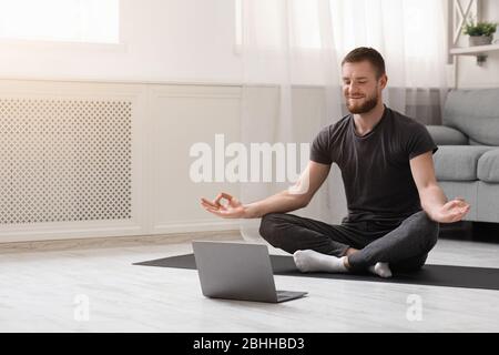 Uomo millenario che medita con il trainer online tramite notebook Foto Stock