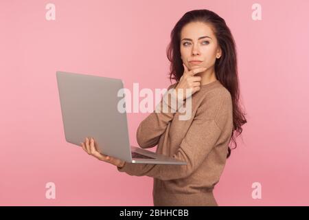 Ispirazione, idea di business. Ritratto di giovane donna in maglione casual tenendo laptop e pensando sulla strategia di avvio con espressi seri dubbi Foto Stock