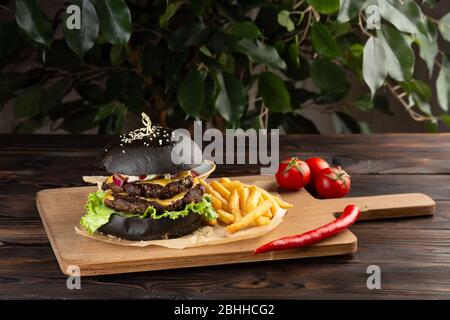 hamburger nero mamba con manzo marmorizzato con patatine fritte, peperoncino e pomodori su un tavolo di legno Foto Stock