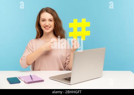 Promozione di pagine Web, tendenze virali. Felice donna sorridente che indica il simbolo giallo grande hashtag, seo smm marketing manager che lavora su notebook in ufficio a casa. Foto Stock