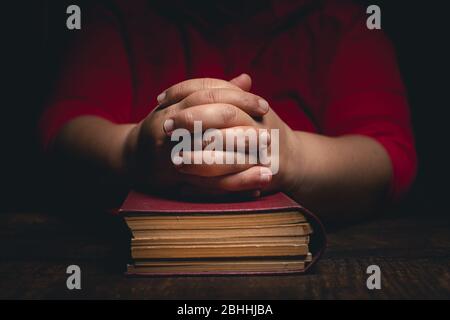Donna con mani chiuse sulla Sacra bibbia, che rimane a casa e prega per la protezione ageainst coronavirus covid-19 pandemi concetto. Foto Stock