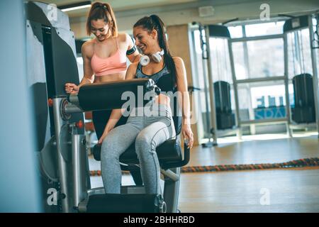 Donna giovane graziosa che ha esercitazioni sull'estensione della gamba e sulla macchina del riccio della gamba nella palestra Foto Stock