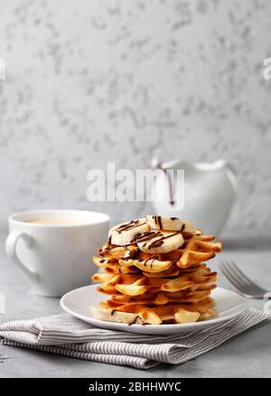 Waffle belgi con salsa di banana e cioccolato su sfondo grigio Foto Stock