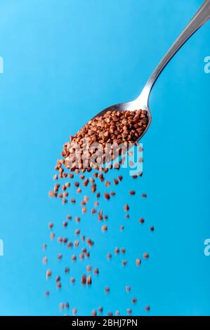 Cereali biologici grani. Semi di grano saraceno crudo che cadono dal cucchiaio su sfondo blu Foto Stock