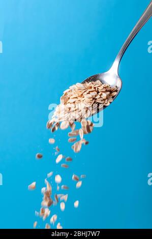 Cereali biologici grani. Fiocchi di farinata d'avena cruda che cadono dal cucchiaio su sfondo blu Foto Stock