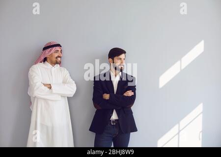Gli uomini d'affari arabi ed europei stanno sorridendo al muro grigio. Le persone multietniche si trovano su uno sfondo grigio. Foto Stock
