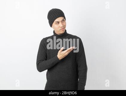 Giovane uomo asiatico bello che indossa maglione grigio e beanie che punta al lato con le mani per presentare un prodotto o un'idea su sfondo bianco. Foto Stock