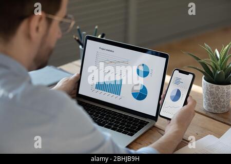 Primo piano uomo d'affari che lavora con le statistiche su laptop e telefono Foto Stock