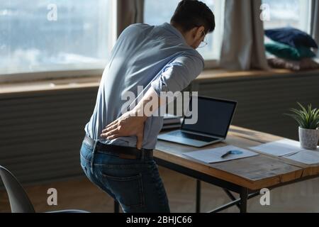 Giovane uomo con vista posteriore che soffre di brusche mal di schiena sul posto di lavoro Foto Stock