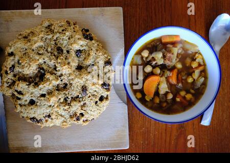 Pane irlandese (con uvetta) su un tagliere, accanto a una ciotola di fagioli e stufato di verdure. Fantastico! Foto Stock