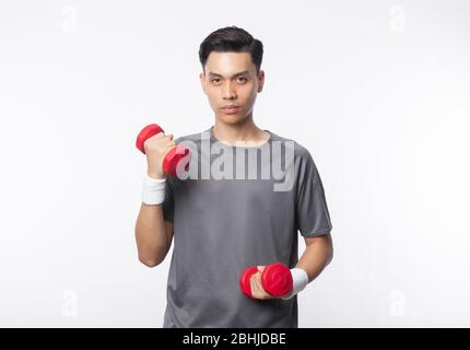 Giovane uomo asiatico in abiti sportivi allenarsi con manubri e cercando di macchina fotografica isolato su sfondo bianco. Foto Stock