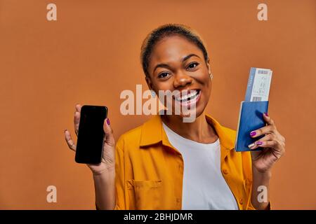 Signora con orecchini con un sorriso con un telefono con passaporto con biglietti. Foto Stock