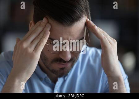 Primo piano uomo stressato malsano che tocca la fronte, soffrendo di mal di testa Foto Stock