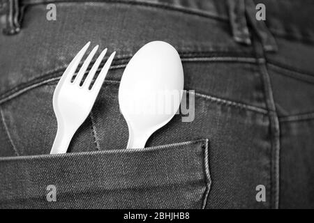 Scopri il concetto di cibo con i jeans denim blu con forchetta bianca e cucchiaio in tasca. Cucchiaio e forchetta in plastica riutilizzabili in tasca. Ambiente sicuro Foto Stock