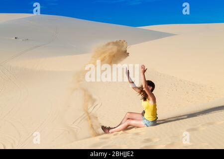 Una donna nel deserto, seduta sulla sabbia, sola, getta sabbia in cima Foto Stock