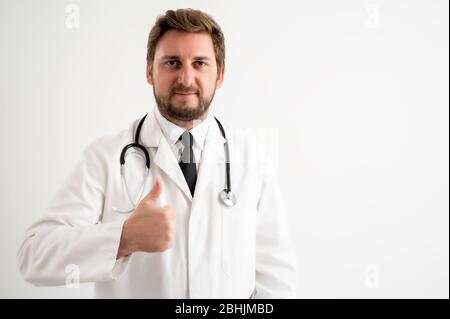 Ritratto di medico maschile con stetoscopio in uniforme medica che mostra pollici in posa su un fondo bianco isolato Foto Stock