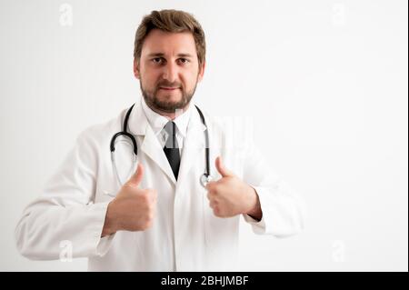 Ritratto di medico maschile con stetoscopio in uniforme medica che mostra pollici su con entrambe le mani in posa su un fondo bianco isolato Foto Stock