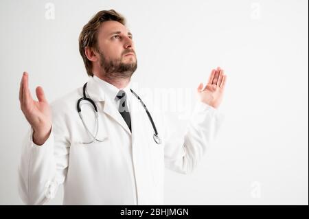 Ritratto di medico maschile con stetoscopio in uniforme medica con braccia aperte in alto, vista laterale in posa su un fondo bianco isolato Foto Stock