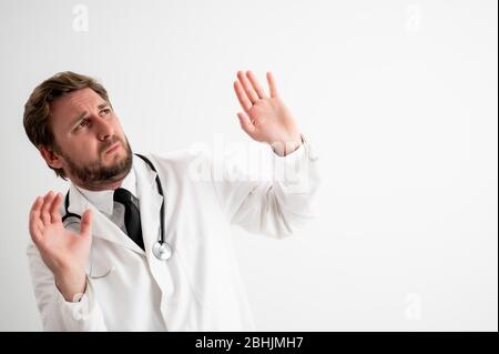 Ritratto di medico maschile con stetoscopio in uniforme medica mostrando paura, con le braccia in posa su un bianco isolato sfondo Foto Stock