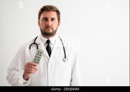 Ritratto di medico maschile con stetoscopio in uniforme medica che mostra le droghe verdi che posano su un fondo bianco isolato Foto Stock