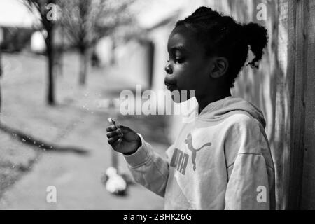 Una foto in bianco e nero di una bambina nera che soffia un dente di leone in una calda giornata estiva Foto Stock