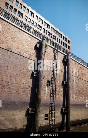 Pali e scala in legno in un canale di Amburgo, accanto a un muro su palafitte Foto Stock