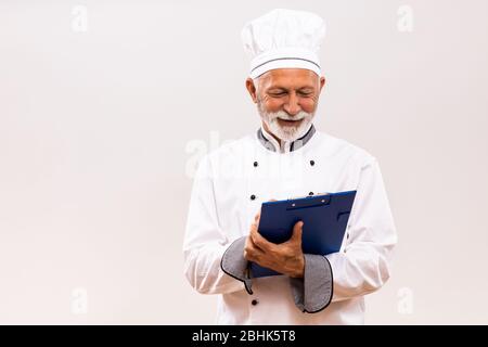 Ritratto dello chef senior che tiene un libro di cucina su sfondo grigio. Foto Stock