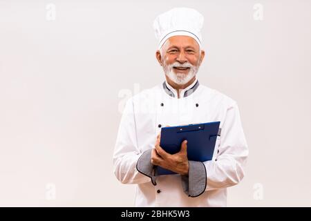 Ritratto dello chef senior che tiene un libro di cucina su sfondo grigio. Foto Stock