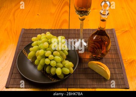 grande spazzola di uva verde in un piatto di ceramica, un decanter e un bicchiere di vino e formaggio Foto Stock