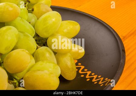 grande spazzola di uva verde in un piatto di ceramica scuro su uno sfondo di legno Foto Stock