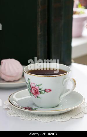 Tè in una tazza d'annata, marshmallows su un piattino d'annata e vecchi libri su uno sfondo chiaro. Foto Stock