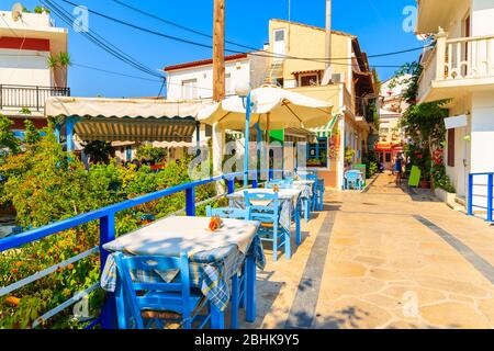 Tavoli con sedie in taverna tradizionale greca sulla strada della città di Kokkari, Grecia Foto Stock