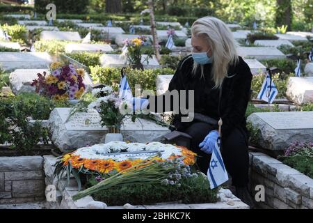 Gerusalemme, Israele. 26 aprile 2020. Una donna israeliana che indossa una maschera protettiva a causa delle piaghie pandemiche del coronavirus COVID-19 sulla tomba di una persona amata al cimitero militare di Mount Herzl a Gerusalemme, mentre Israele si prepara a celebrare il giorno commemorativo per i soldati caduti. Le cerimonie ufficiali non si svolgeranno quest'anno a causa di un coprifuoco nazionale per combattere la pandemia COVID-19. Foto Stock