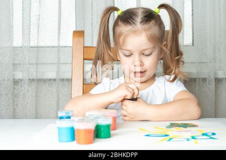 cosa fare per un bambino durante il periodo di quarantena e di autoisolamento, 4 anni ragazza apre un vaso di gouache e sorrisi. di fronte a esso sono molti Foto Stock