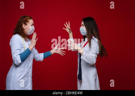 Ritratto di due medici femminili in abiti medici con fonendoscopio intorno al collo si stanno discutendo, immagine isolata su sfondo rosso Foto Stock