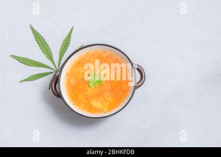 Zuppa infusa di marijuana in una ciotola con foglia di cannabis su sfondo grigio neutro, spazio per testo Foto Stock