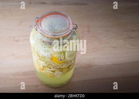 Vaso di vetro ermetico riempito con sambuco e fette di limone combinati per rendere casalingo sciroppo di sambuco o cordiale, una deliziosa bevanda estiva. Foto Stock