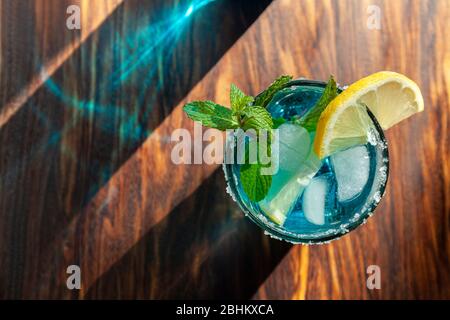Cocktail alcolico blu in un bicchiere su un bancone bar in legno Foto Stock