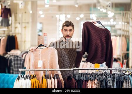 Un giovane che aiuta la sua ragazza a trovare il maglione giusto in un negozio di abbigliamento. Foto Stock