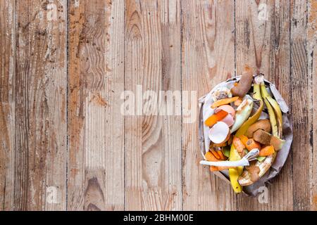 Rifiuti organici in un sacchetto di carta su uno sfondo di legno con spazio per il testo. Vista dall'alto. Concetto ecologico di rifiuti biologici. Foto Stock