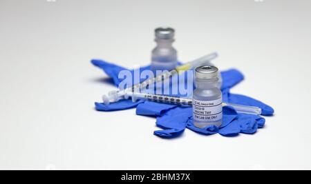 Un paio di flaconcini di vaccino di prova Covid-19 sopra i guanti per uso medico in gomma blu con siringhe. Foto Stock