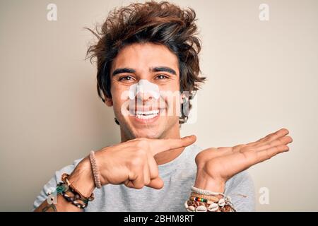 Giovane uomo bello che usa la striscia del naso in piedi su sfondo bianco isolato stupito e sorridente alla macchina fotografica mentre presenta con la mano e puntando w Foto Stock