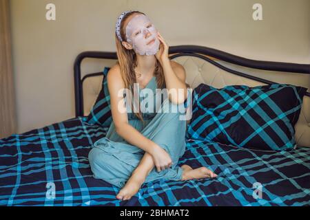 I giovani i capelli rossi donna facendo maschera facciale foglio. Bellezza e cura della pelle Concept Foto Stock