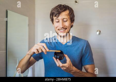 Giovane uomo spazzola i denti usando polvere di carbone Attivata per spazzolare e sbiancare i denti. Spazzola ecologica di bambù Foto Stock