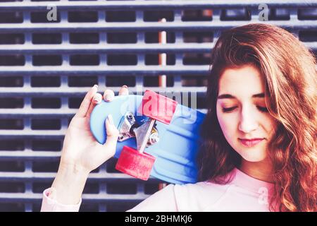 Immagine di contrasto di una ragazza con uno skateboard sulla spalla e gli occhi chiusi. CopySpace. Foto Stock