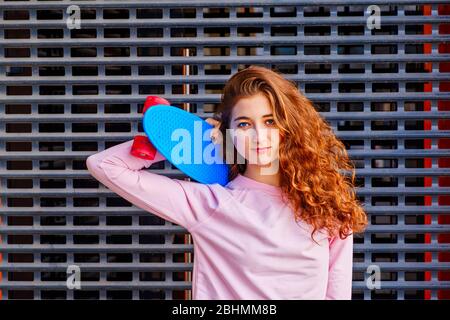 l'immagine di una ragazza con uno skateboard sulla spalla contro lo sfondo di una rete di protezione in metallo in un parco skateboard Foto Stock