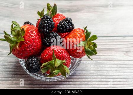Vista su una piccola ciotola di vetro piena di fragole e more. Messa a fuoco selettiva. Foto Stock