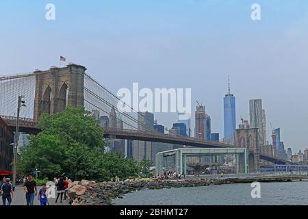 New York, USA - 05 giugno 2019: Folla di turisti e persone locali a piedi nel parco del ponte di Brooklyn accanto al fiume Est a New York con il ponte di Brooklyn. Foto Stock